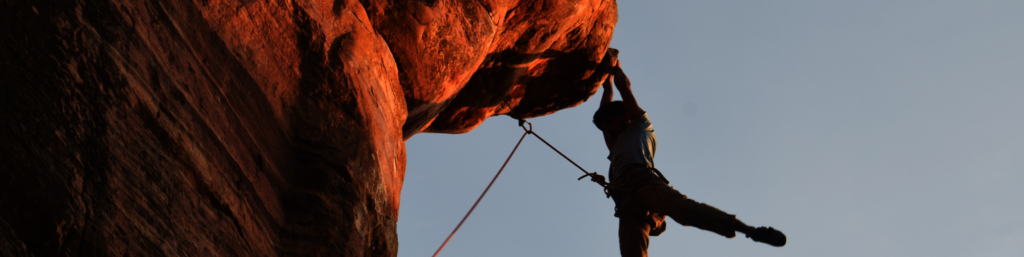 A man climbing on a red rock wall with a rope and his bare hands.