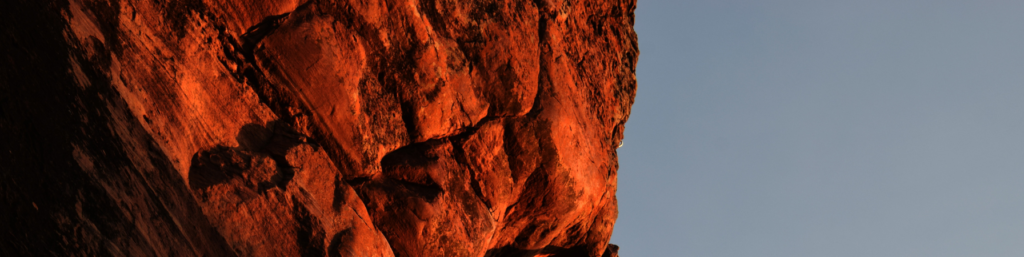 A man climbing on a red rock wall with a rope.