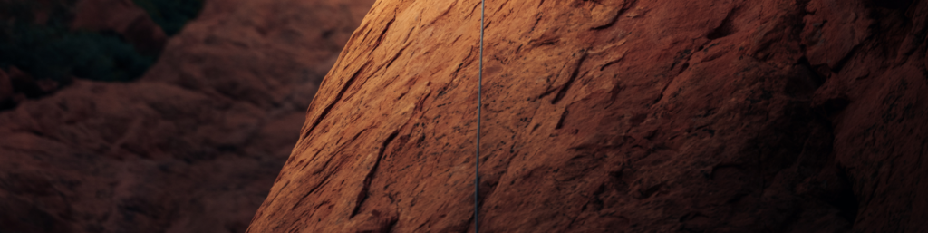 Illuminated red rock wall with a climbing cable.