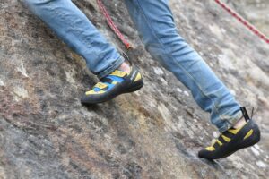 Legs of a person climbing a rock, wearing blue pants and sustainable made climbing shoes.